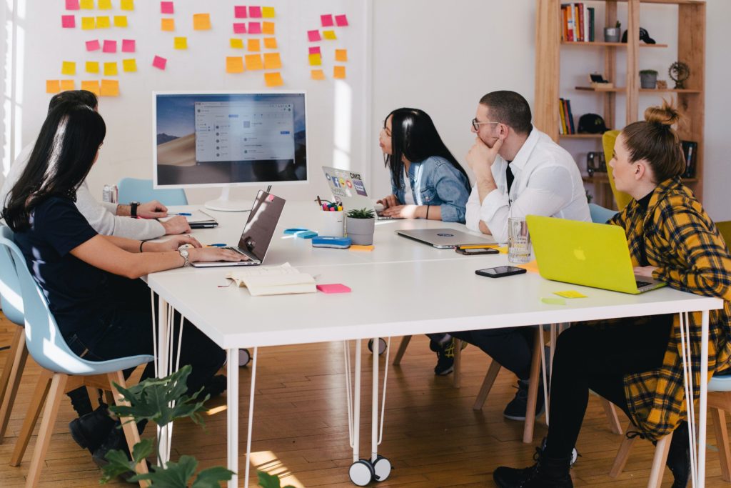 Group of individuals brainstorming at a desk with laptops and notepads on it.