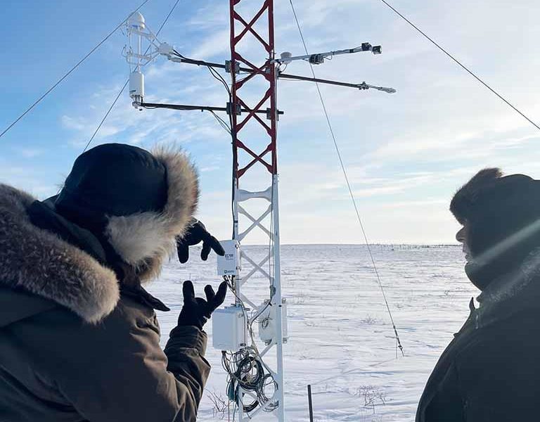 people in winter jackets looking at a tower in Inuvik