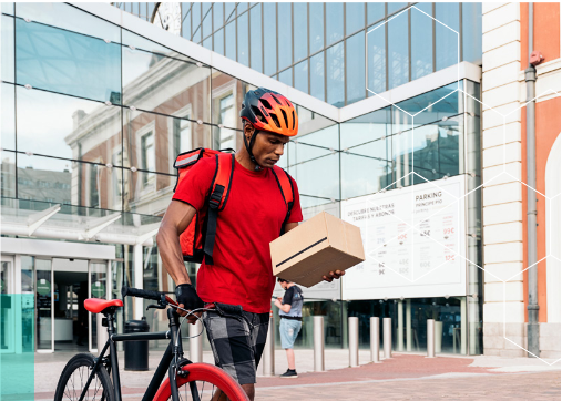 Bicycle delivery person in red t-shirt and orange helmet holding a brown package next to their bike