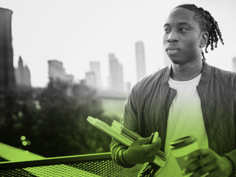 Young man carrying books with a city skyline in the background.