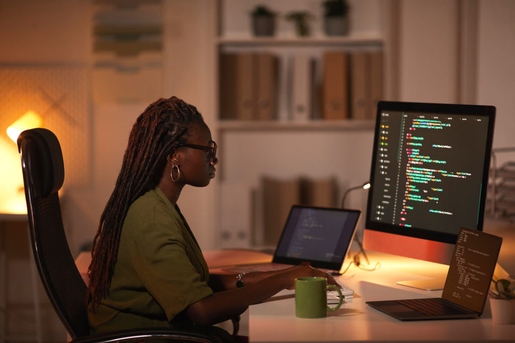 Person coding on their computer in an office at night, with multiple monitors in front of them.