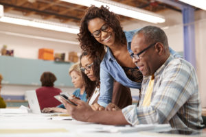Teacher Helping Retired Senior Man Attending IT Class In Community Centre