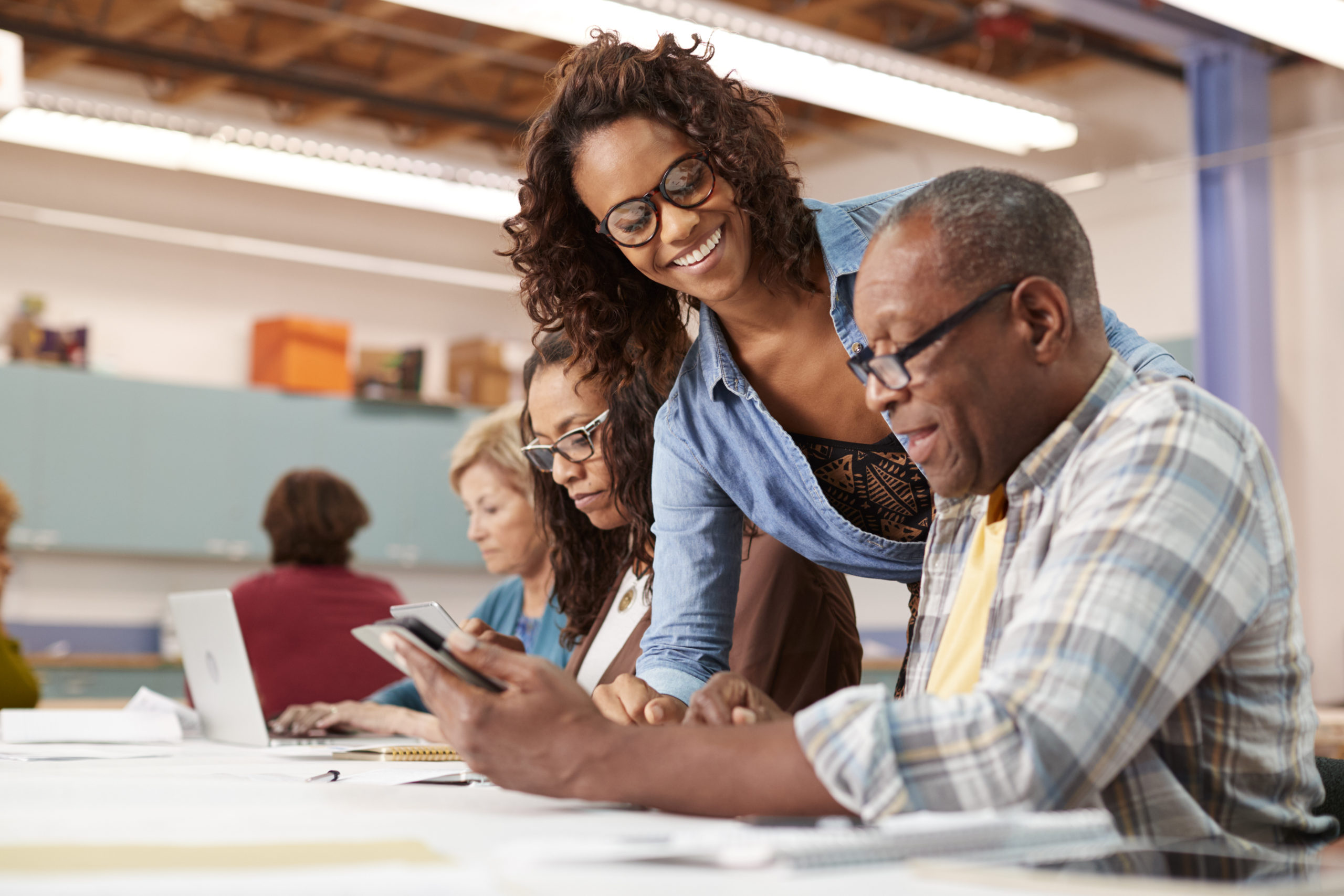 Teacher Helping Retired Senior Man Attending IT Class In Community Centre