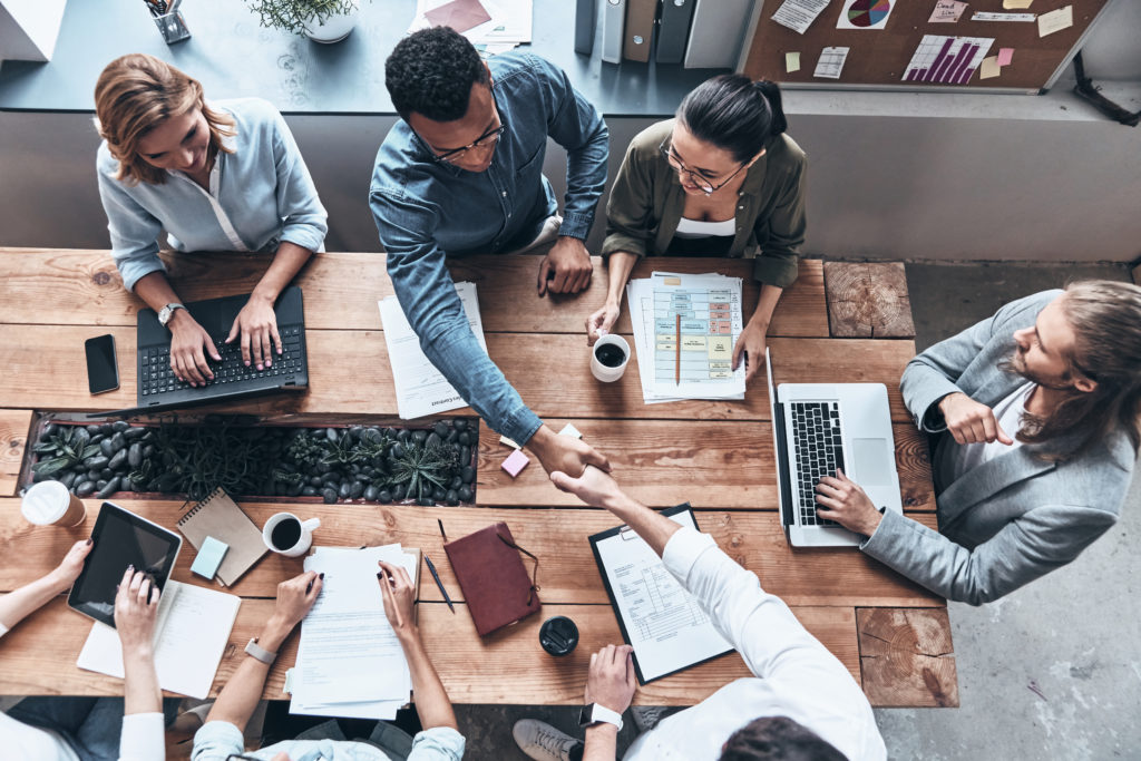 Top view of young modern men in smart casual wear shaking hands while working in the creative office