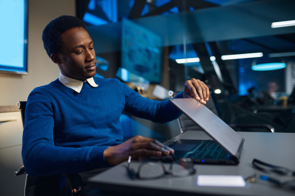 Tired manager closing laptop, night office lifestyle. Male person at the table, dark business center interior on background, modern workplace