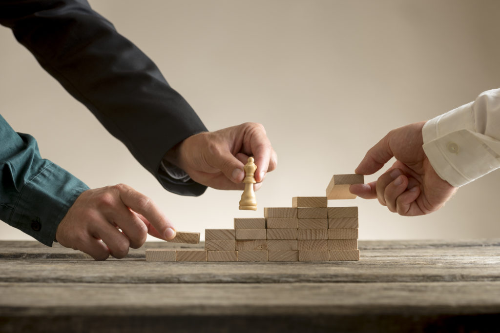 Business teamwork concept with a businessman moving a chess piece queen up a series of steps formed by blocks being put in place by his team.