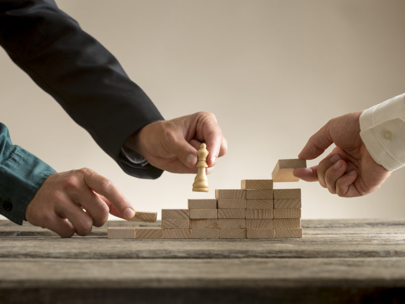 Business teamwork concept with a businessman moving a chess piece queen up a series of steps formed by blocks being put in place by his team.