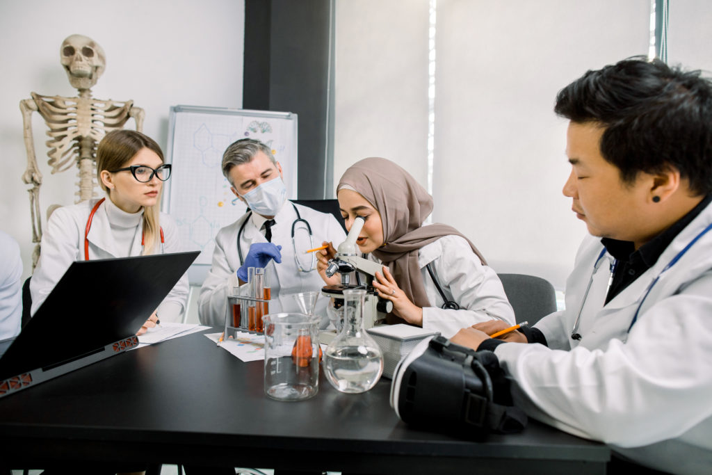 science, chemistry, microbiology, medicine concept. Multiethnical scientists working with microscope, flasks and tubes making test or research in clinical laboratory. Muslim woman uses microscope.