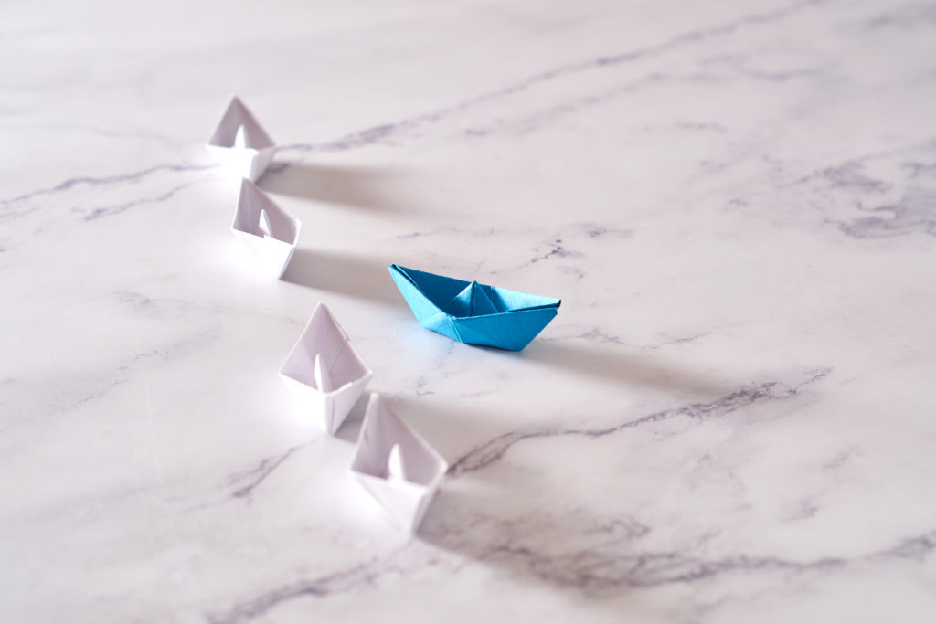Think different - individuality concept, paper boat going to opposite side
