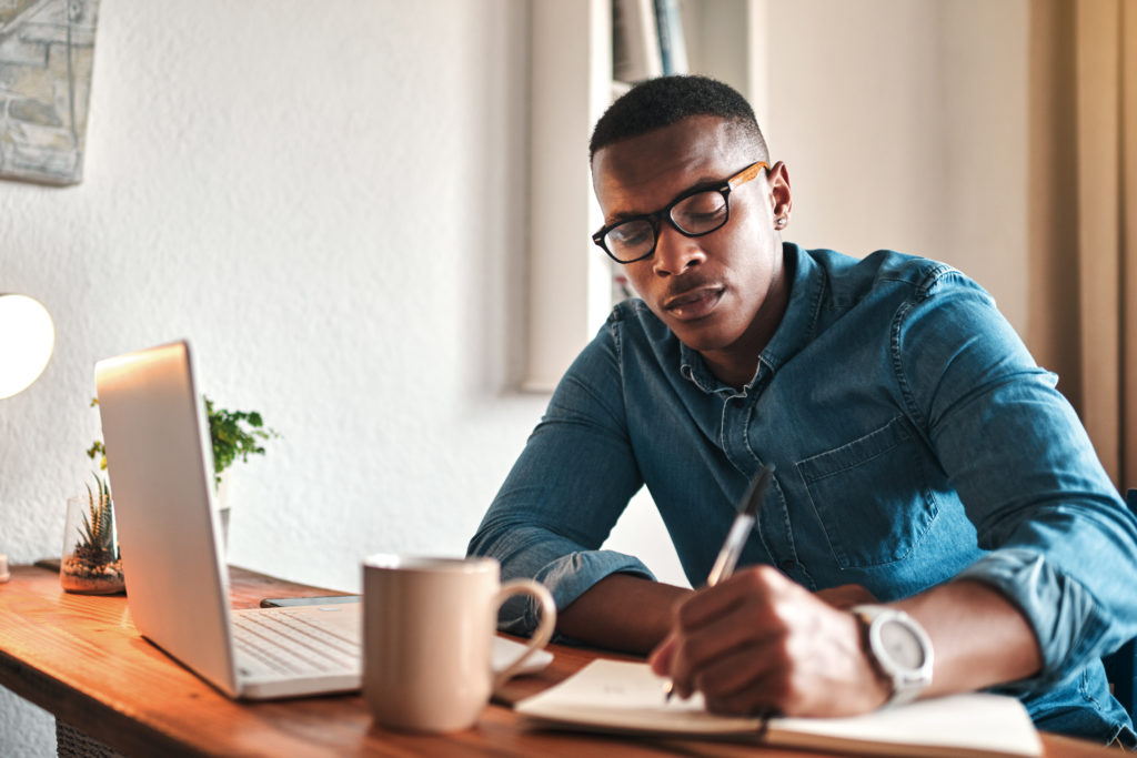 Cropped shot of a young businessman sitting alone in his home office and writing notes.