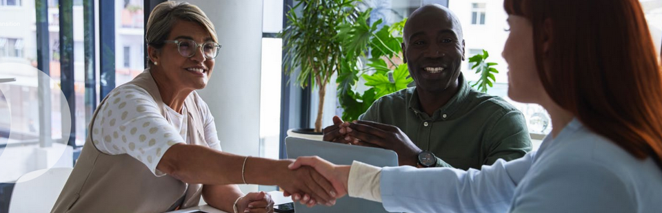 A group of three people where two are shaking hands and smiling.