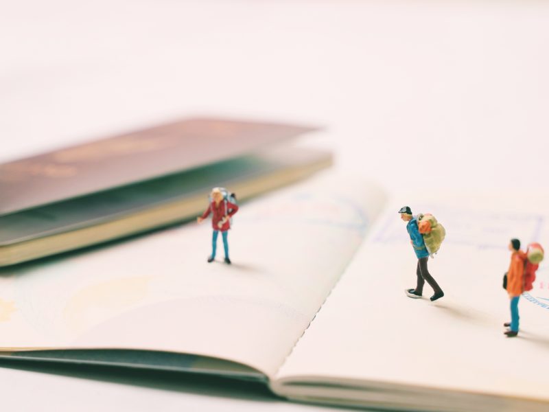 Miniature people figures with backpack walking and standing on passport page with immigration stamps, travel and vacation concept