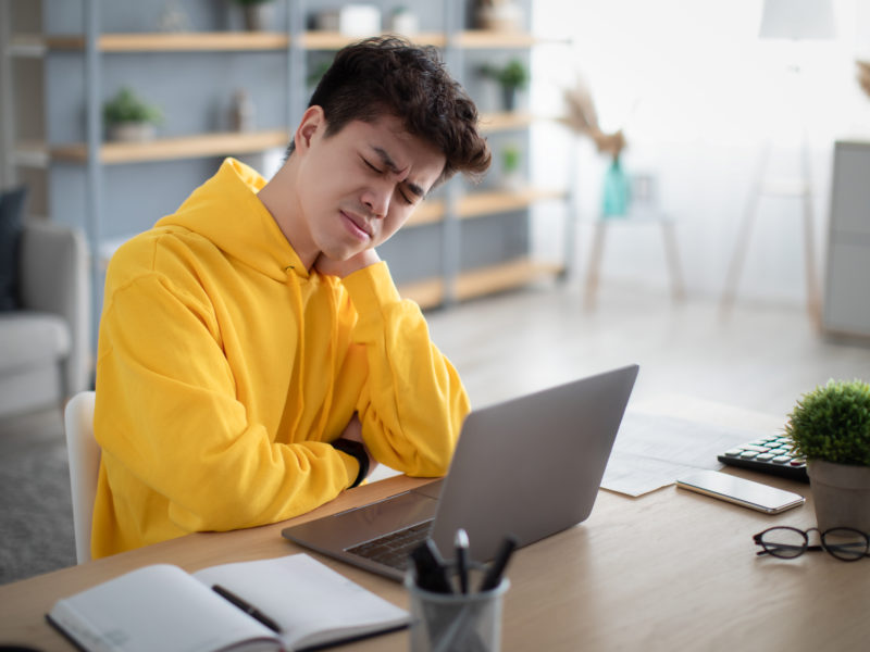 Neck Pain. Exhausted Asian Man Massaging Aching Neck Suffering From Ache Sitting Working At Laptop At Desk In Living Room At Home Office. Osteoarthritis, Health Problem, Sedentary Lifestyle Concept