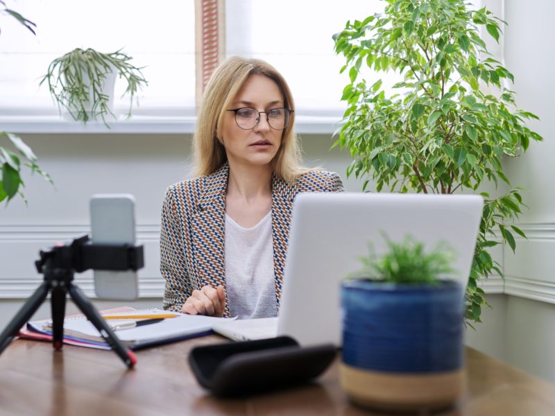 Business woman working at home online using laptop and smartphone. Middle-aged confident female using video call, conference, looking at webcam, business owner, teacher, accountant working remotely