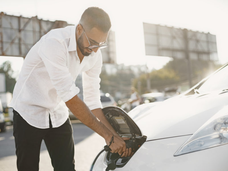 Young adult man charging his electric car in the city