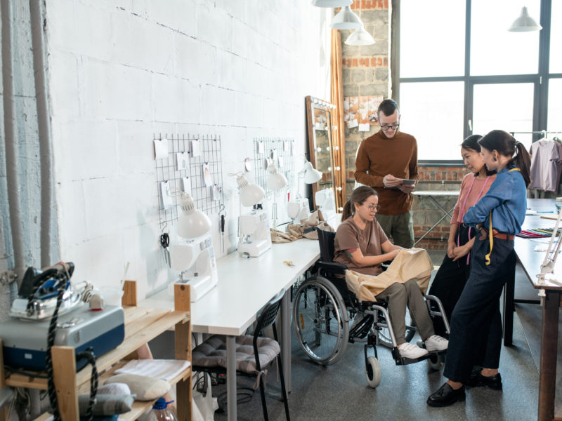 Group of tailors, including one in a wheelchair, consulting during work over new fashion collection