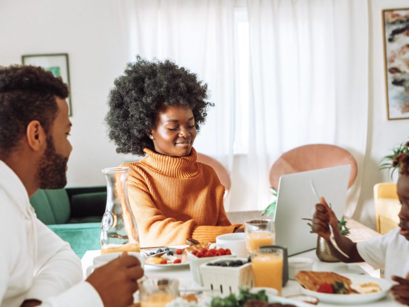 Black family around the breakfast table with woman working on laptop