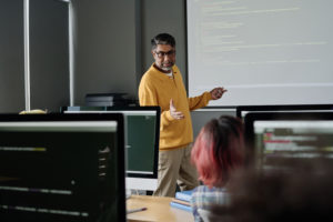 Teacher of Computer Science standing in front of students in modern classroom and conducting lesson