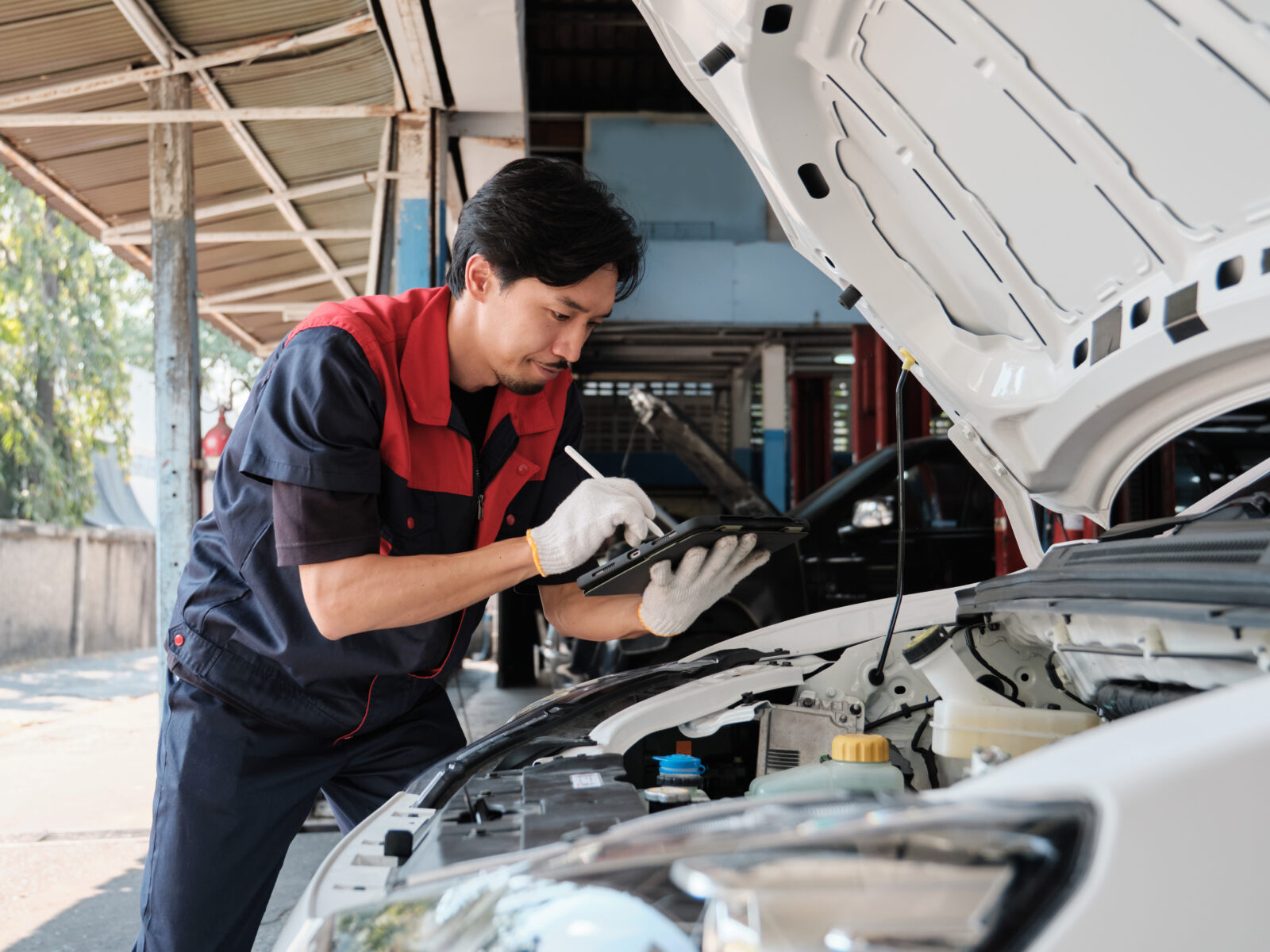 Mechanic worker inspects and maintains service of electric engine and battery in automobile garage