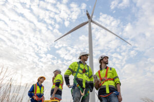 Workers wearing safety uniforms discuss operational planning at wind turbine field