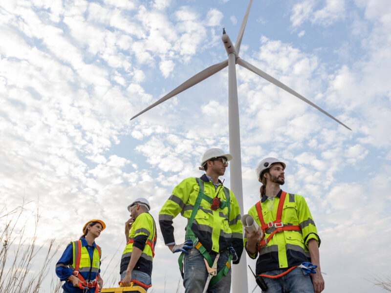 Workers wearing safety uniforms discuss operational planning at wind turbine field