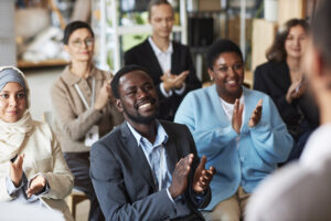Group of people sitting in row in front of speaker and clapping hands