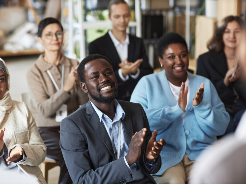 Group of people sitting in row in front of speaker and clapping hands