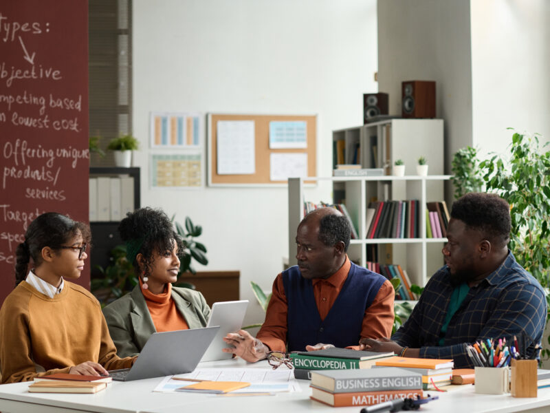 Black professor talking to group of students sitting at table