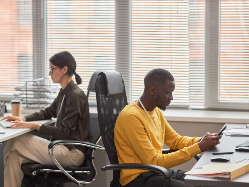 Two office workers at desks back to back working in office