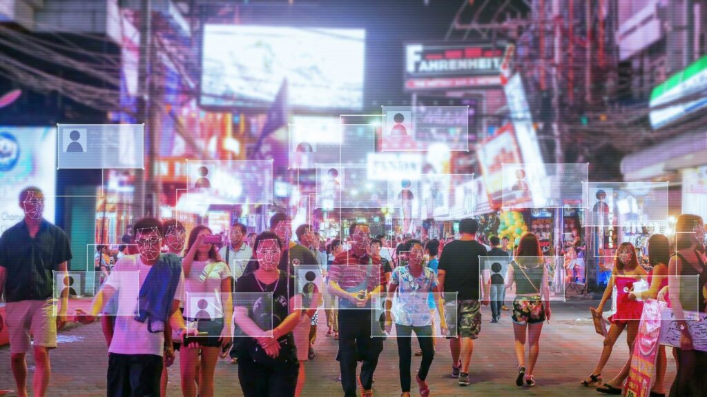Crowded city street at night with digital facial recognition overlays tracking pedestrians