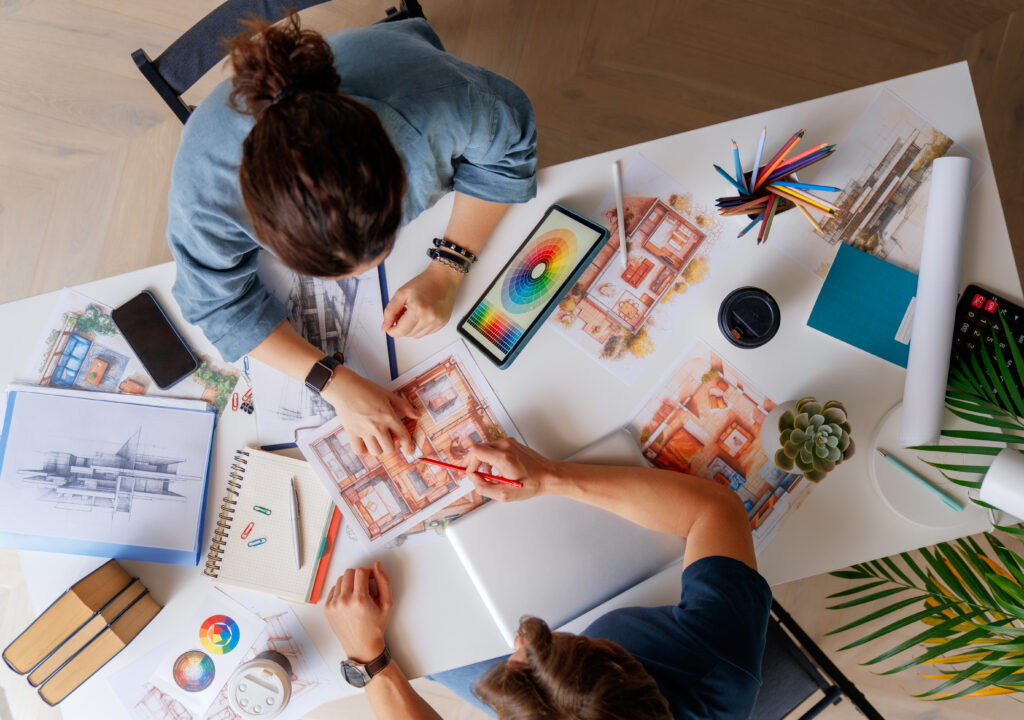 Two people collaborating on interior design sketches at a desk with color swatches and drawings.