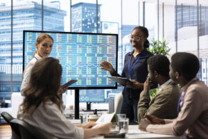 Team reviewing stock market data on a large screen during a business meeting.