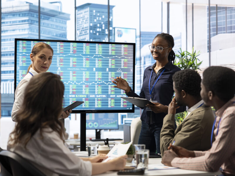 Team reviewing stock market data on a large screen during a business meeting.