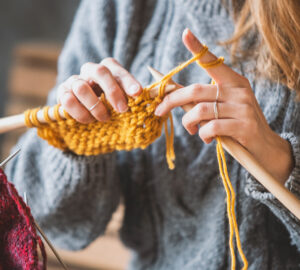 Hands knitting yellow yarn with wooden needles.