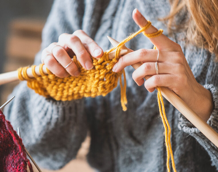 Hands knitting yellow yarn with wooden needles.