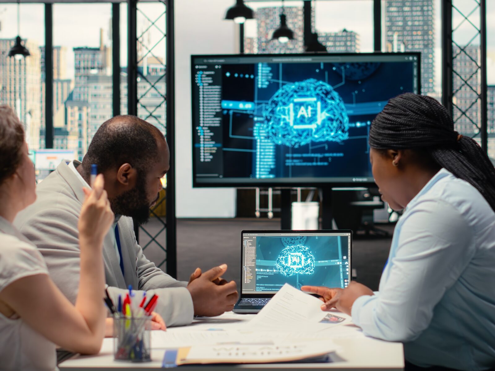 Three professionals in a high-tech office review an AI brain visualization on multiple screens.