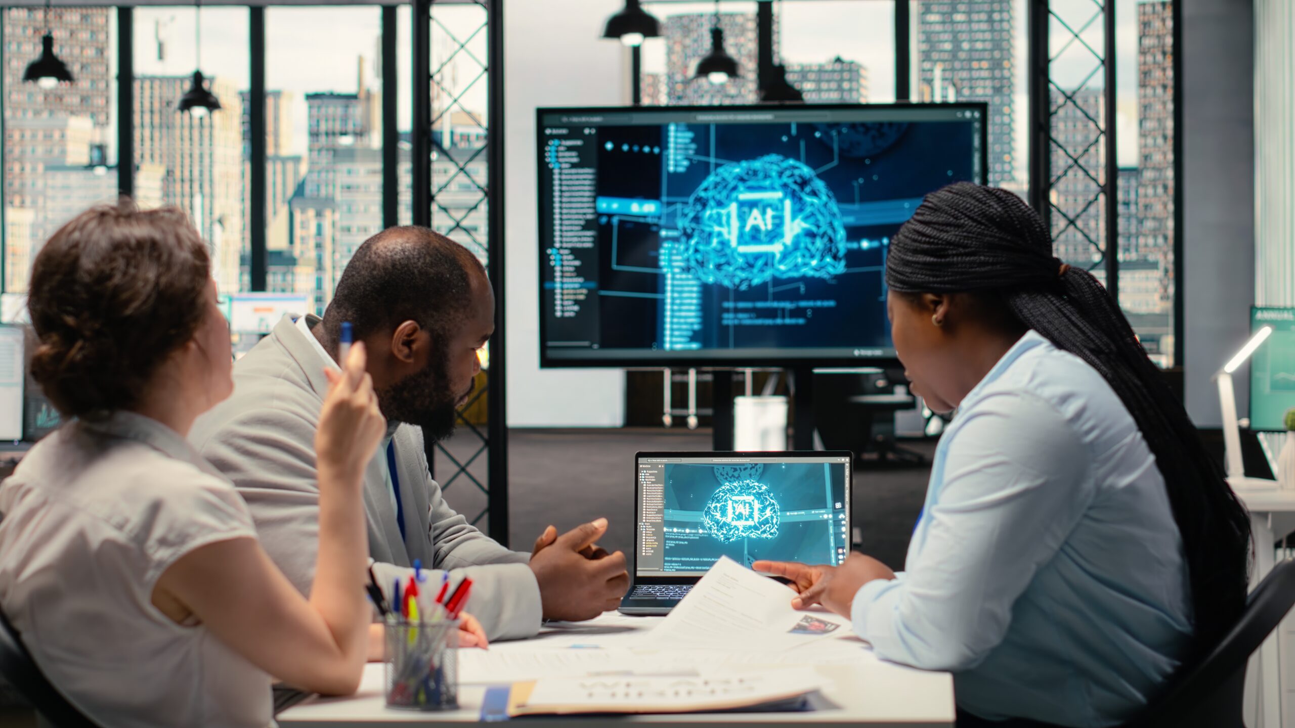 Three professionals in a high-tech office review an AI brain visualization on multiple screens.