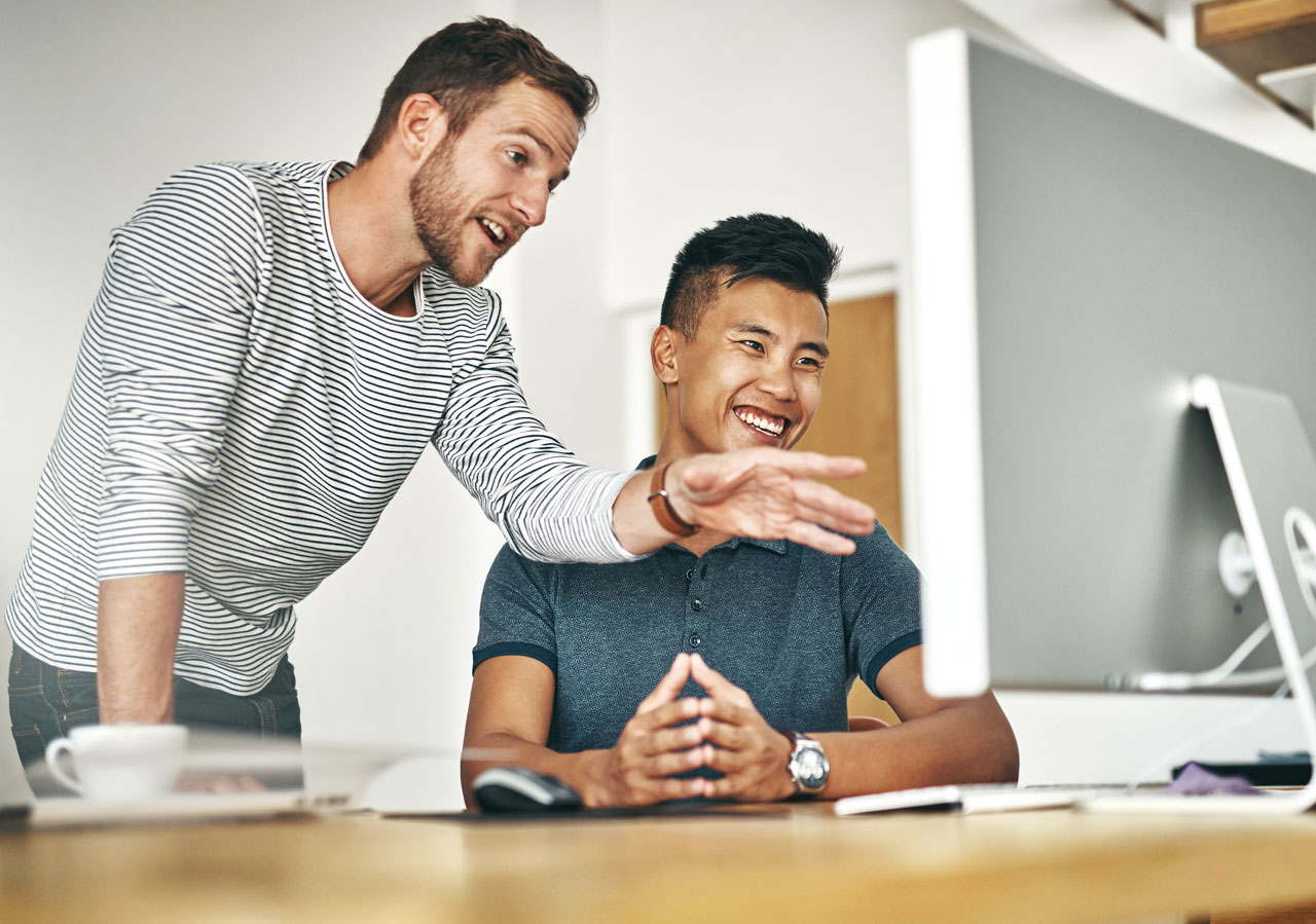 Two coworkers smiling and collaborating at a computer in an office.