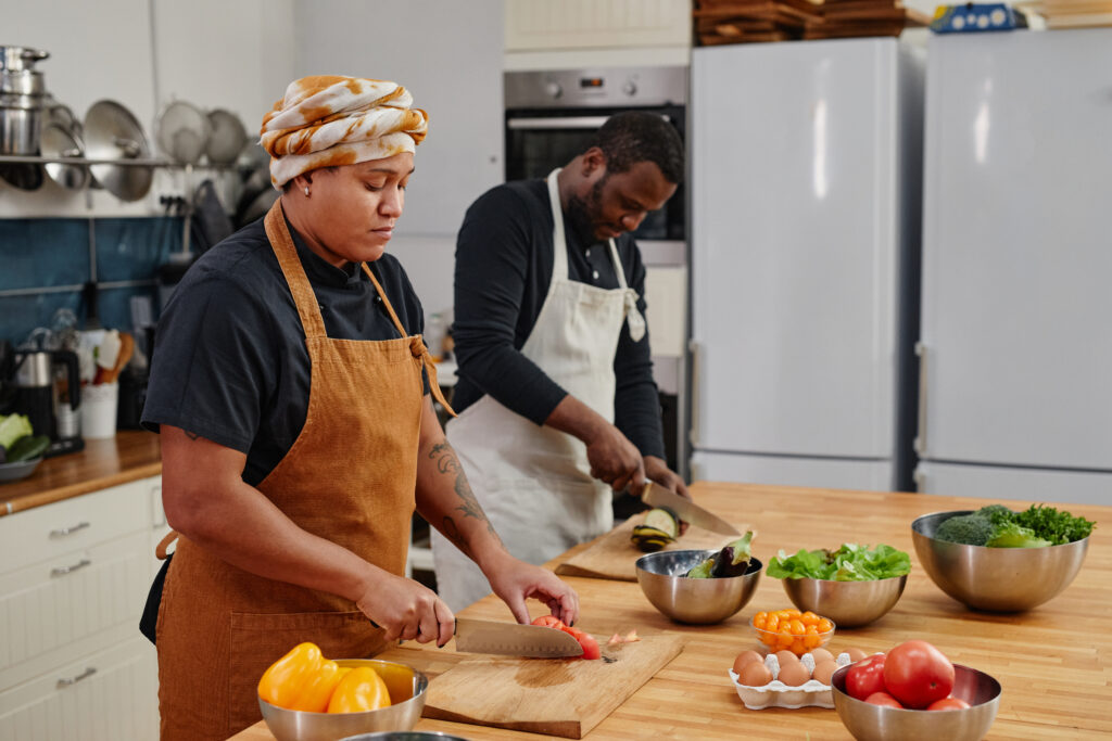 Two chefs working at a wooden kitchen island, preparing fresh vegetables.