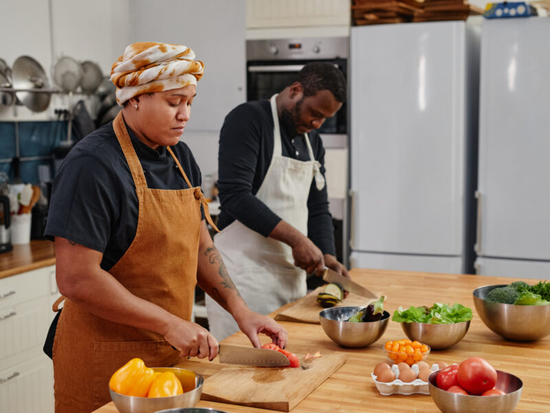 Two chefs working at a wooden kitchen island, preparing fresh vegetables.