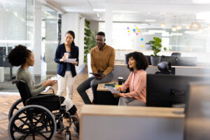 Diverse team members collaborate in a modern office, including a woman using a wheelchair, as they discuss documents and ideas together.