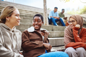 Students sitting on outdoor campus steps, smiling and chatting together between classes.
