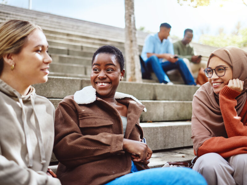 Students sitting on outdoor campus steps, smiling and chatting together between classes.