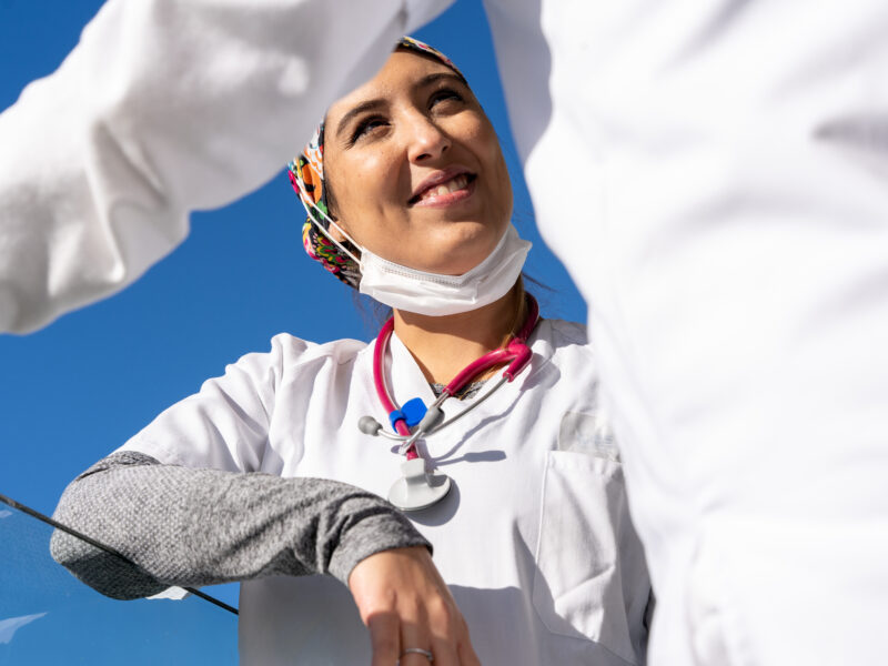 A woman smiles brightly in this waist-up shot taken in a sunny setting.