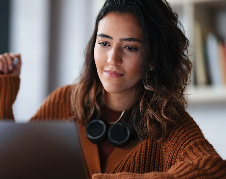 Person wearing headphones around their neck while using a laptop indoors