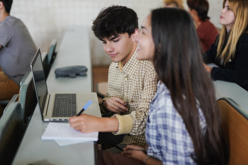 Students working together in a classroom, with a laptop and notebook.