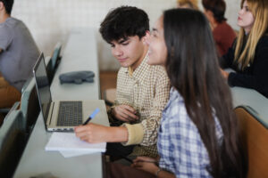 Students working together in a classroom, with a laptop and notebook.