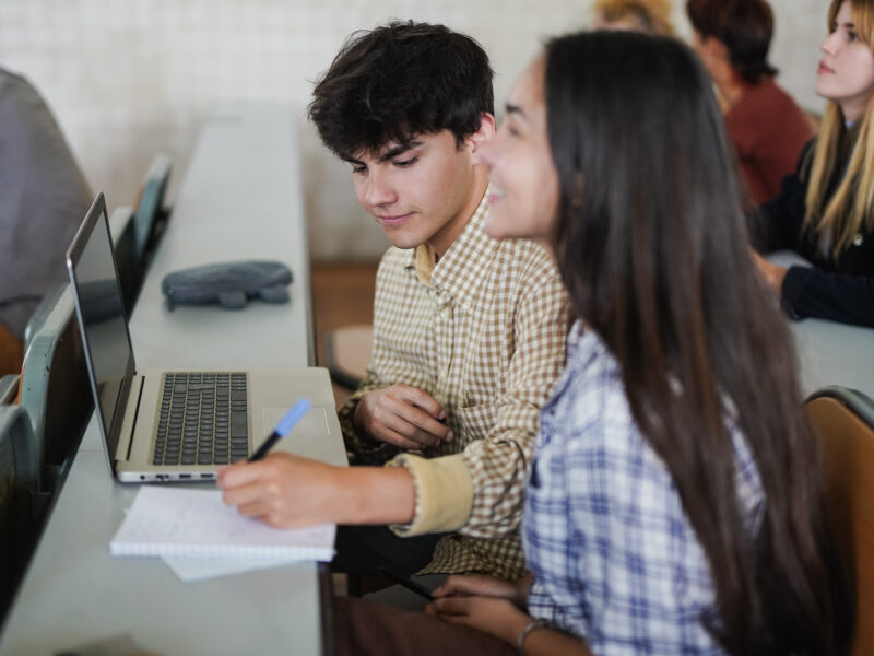 Students working together in a classroom, with a laptop and notebook.