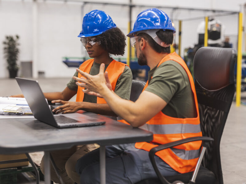 Engineers collaborating on laptop in modern factory setting
